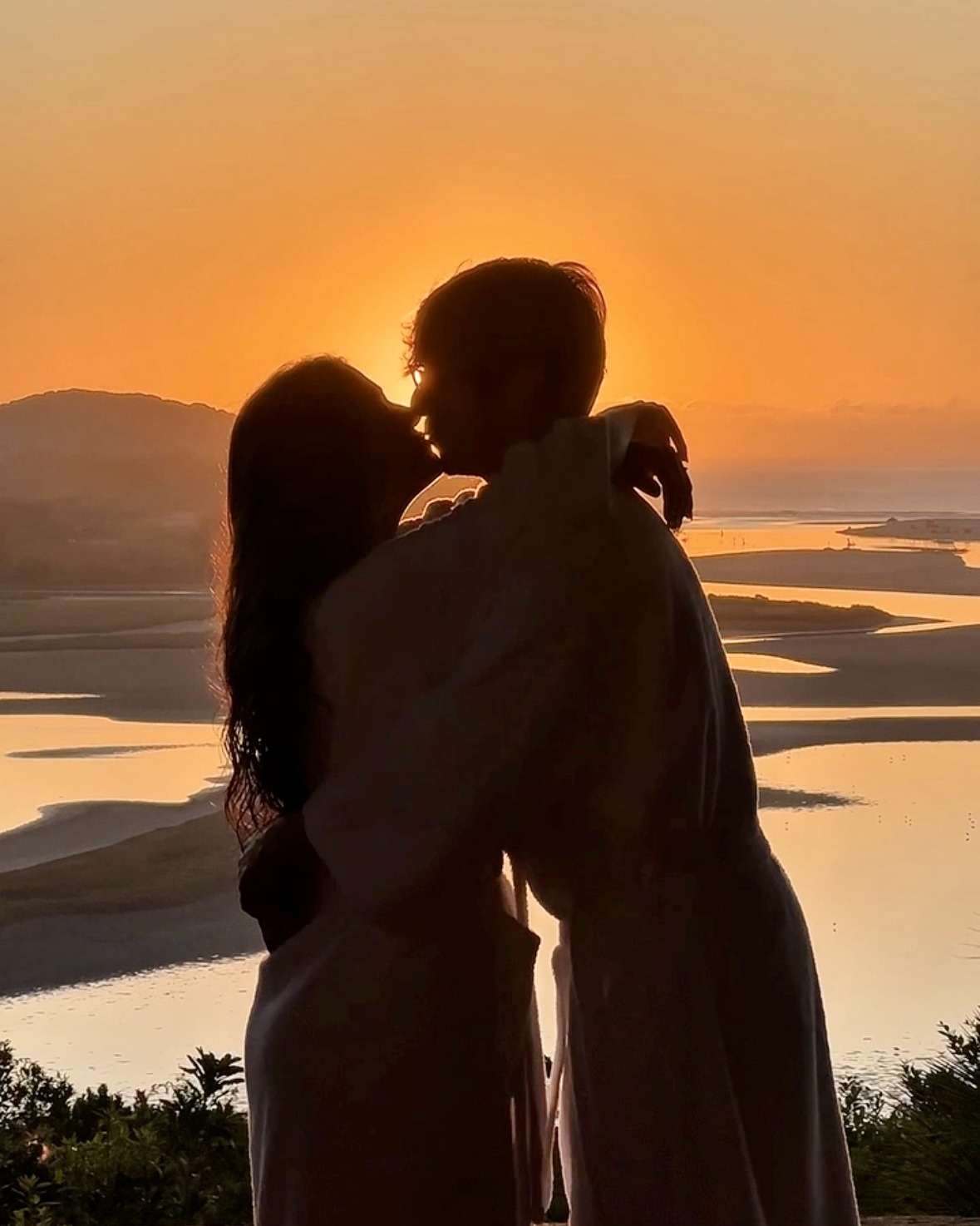 Casal se beijando ao nascer do sol diante da lagoa